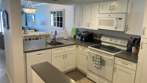 A modern kitchen with white cabinets, a stainless steel countertop, and a built-in microwave. - Ground Floor Direct Oceanfront 2/2 (New Smyrna Beach)