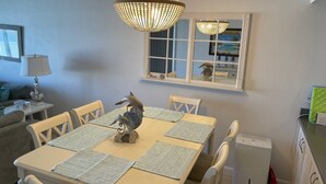 A dining area with a table set for four, a chandelier, a window with a view, and a small table with a lamp. - Ground Floor Direct Oceanfront 2/2 (New Smyrna Beach)