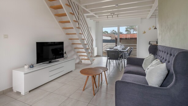 Una sala de estar moderna con una escalera, un televisor de pantalla plana, un sofá gris y un comedor.
