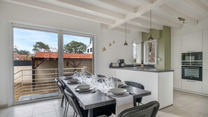 Una cocina moderna con una isla central, un comedor con una mesa larga para seis personas, y un puerta corrediza de vidrio que da a un espacio exterior.