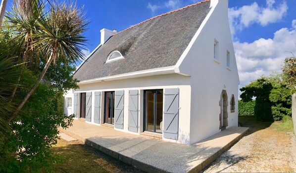 Une maison blanche avec un toit gris, de grandes portes coulissantes et un petit porche.