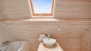 Une salle de bain avec un puits de lumière, une baignoire, un lavabo et un lambris en bois.