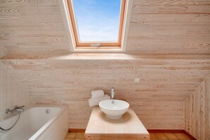 Une salle de bain avec un puits de lumière, une baignoire, un lavabo et un lambris en bois.
