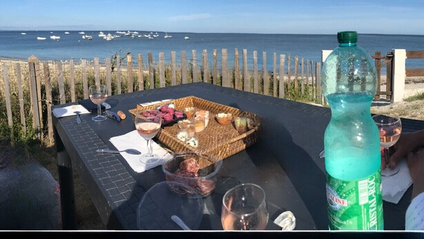 Una mesa con una cesta de mimbre que contiene comida, una botella de Cristal-Roc y copas de vino.