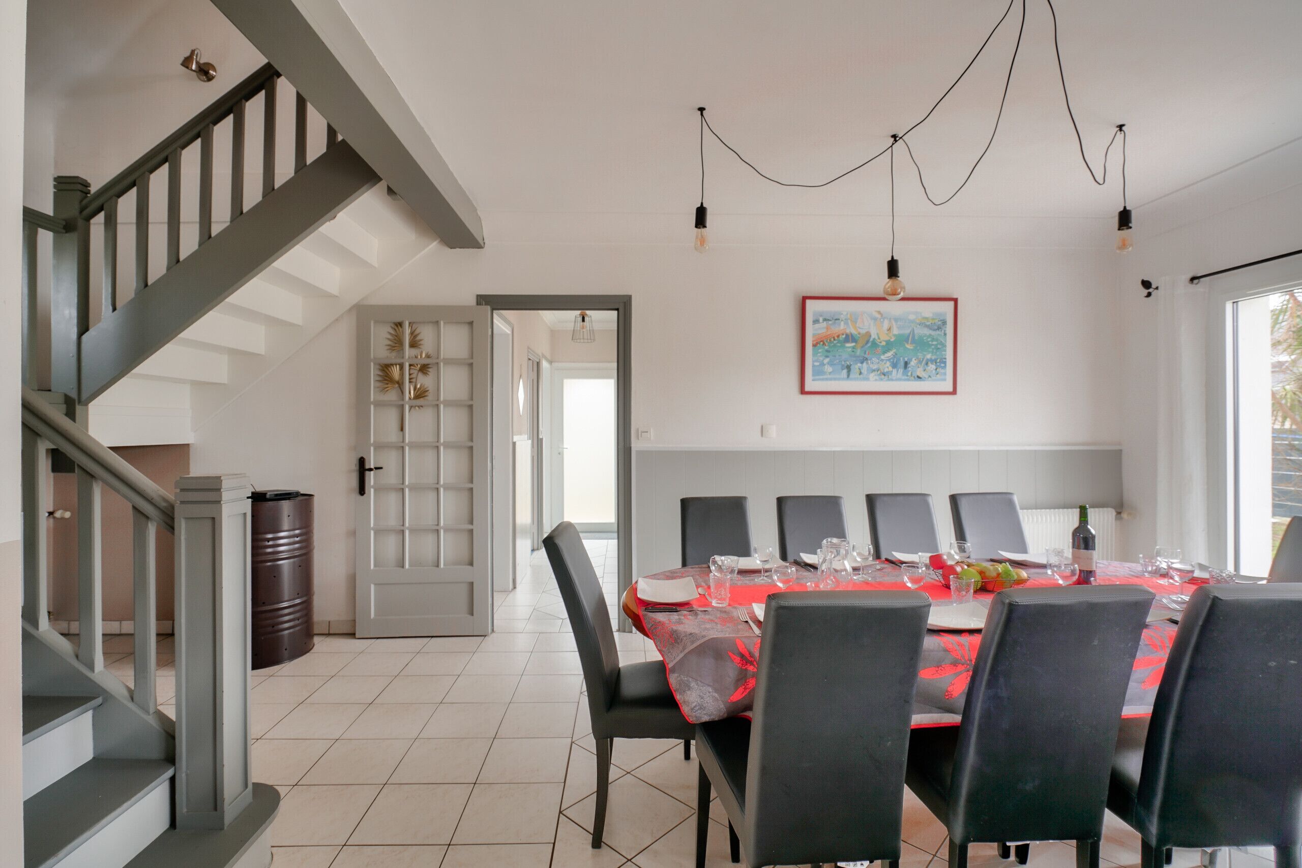 A dining area with a table set for six, a staircase, and a door leading to another room.