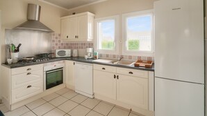 Una cocina con gabinetes blancos, una campana extractora de acero inoxidable, microondas, lavavajillas y refrigerador.