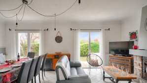 Una sala moderna con sofá, mesa de comedor y televisor. Cuenta con ventanas amplias y una chimenea.