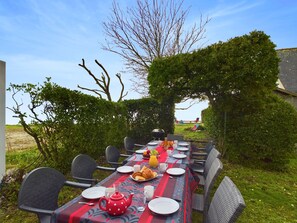 Un espace de restauration en plein air avec une table dressée pour un repas, entourée de chaises et de verdure.