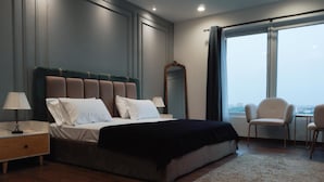 A modern bedroom with a large bed, a nightstand, a mirror, and two chairs.