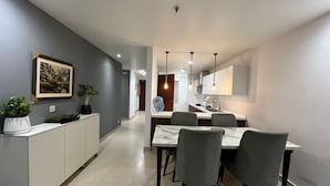 A modern kitchen with white cabinets, a dining area with a marble table, and grey chairs.