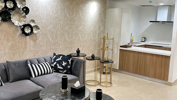A modern living room with a grey sofa, two round tables with gold legs, and a kitchen area with a white countertop and wooden cabinets.