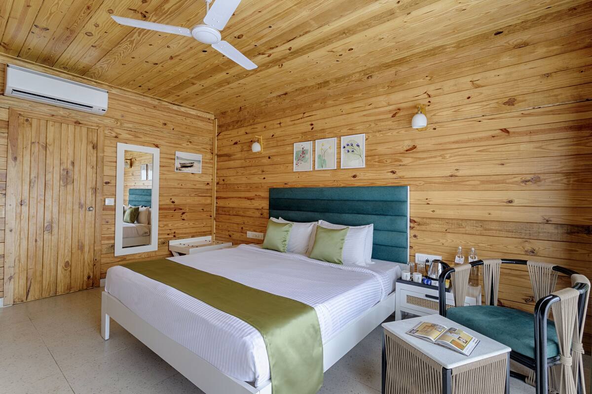 Une chambre à coucher aux murs lambrés, avec un lit, un bureau, une chaise et un ventilateur de plafond.