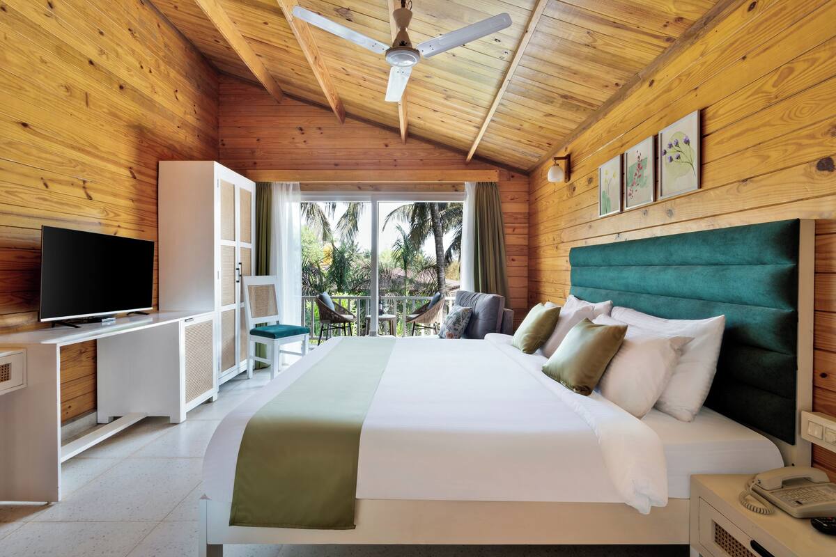 Une chambre dans un chalet en bois, équipée d’un lit, d’une télévision et d’un balcon avec des chaises.