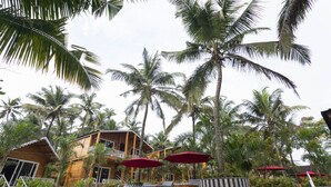 Un resort con piscina, palmeras y edificios de madera con sombrillas rojas.