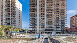 A multi-story hotel with balconies, a pool area, and a beach view.