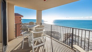 A balcony with a table and chairs, overlooking a beach and ocean.