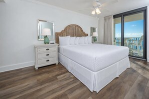 A hotel room with a large bed, a nightstand, a mirror, a ceiling fan, and a balcony with a view.