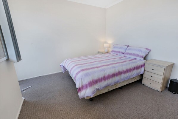Un dormitorio con cama, mesita de noche con lámpara y cómoda de madera.