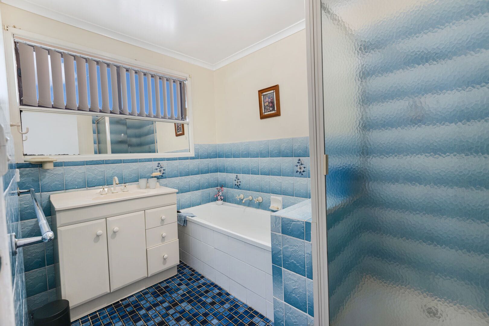 A bathroom with a white vanity, a bathtub, and blue-tiled walls.
