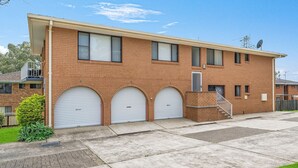 A two-story brick building with three garage doors, a satellite dish, and a small staircase leading to a second-floor entrance. - Bridgeview - Relaxing Getaway Near Surf Beach, Lake and Sand (Lake Cathie)