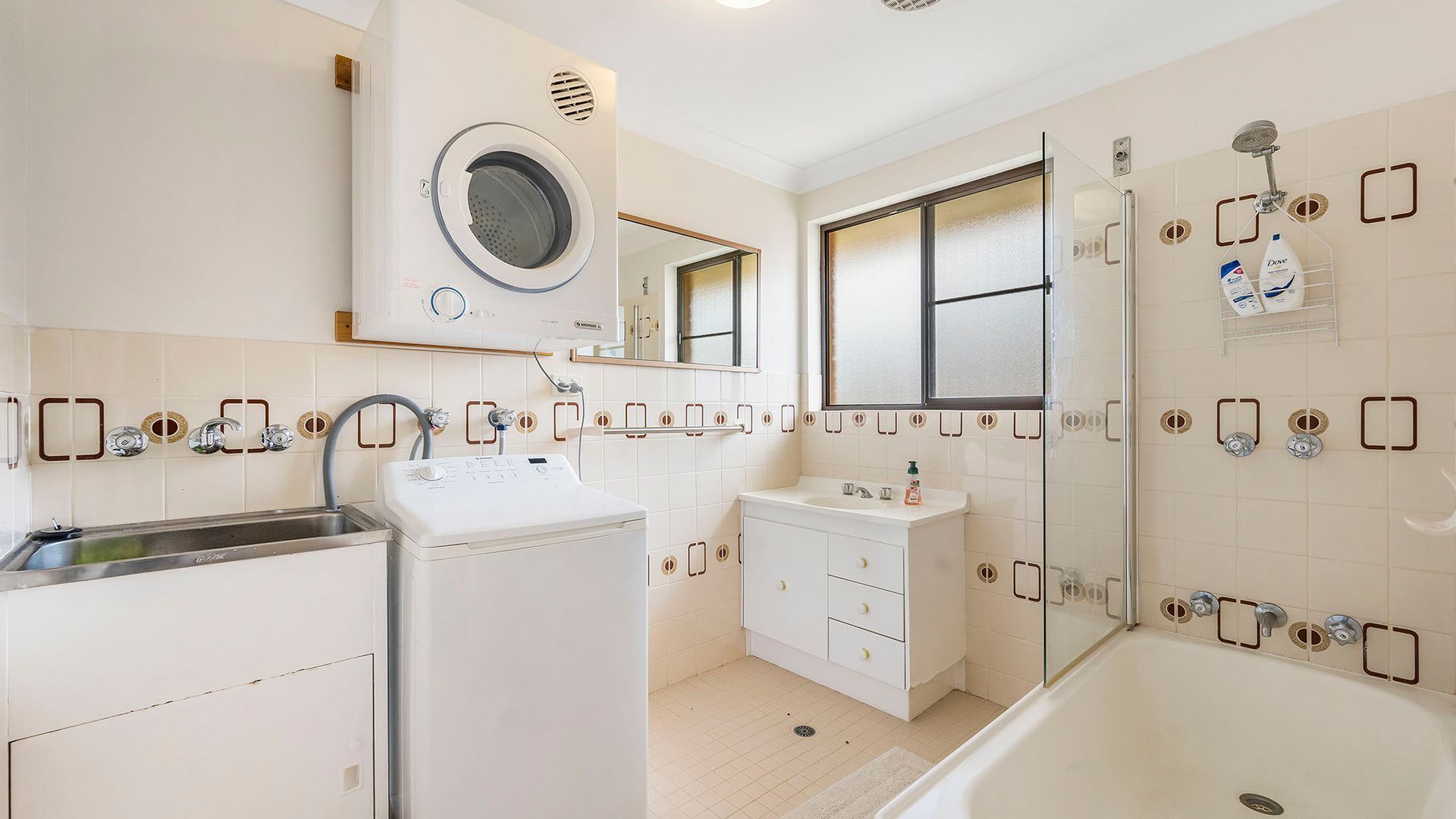 A modern bathroom with a built-in washing machine, a glass shower enclosure, and a vanity with a mirror.