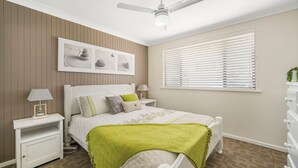 A bedroom with a bed, bedside tables, a ceiling fan, a window with blinds, and a wall-mounted artwork. - Bridgeview - Relaxing Getaway Near Surf Beach, Lake and Sand (Lake Cathie)
