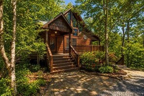 A cabin with a wooden exterior, a front porch, and a staircase leading to the entrance.