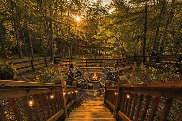 A wooden deck leading to a fire pit area surrounded by a forest.