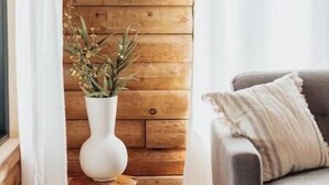 A rustic interior with a wooden wall, a cow skull mounted above a white vase with dried flowers, and a grey sofa with a white cushion. - Beautiful Log Cabin, Pond adjacent on Big Bear Golf Course  (Big Bear Lake)