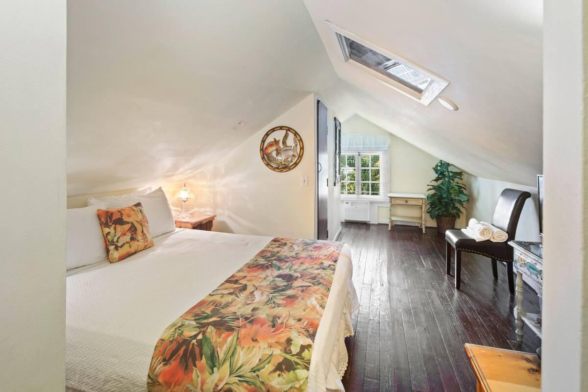 A bedroom with a bed, a bench, a desk, and a potted plant.