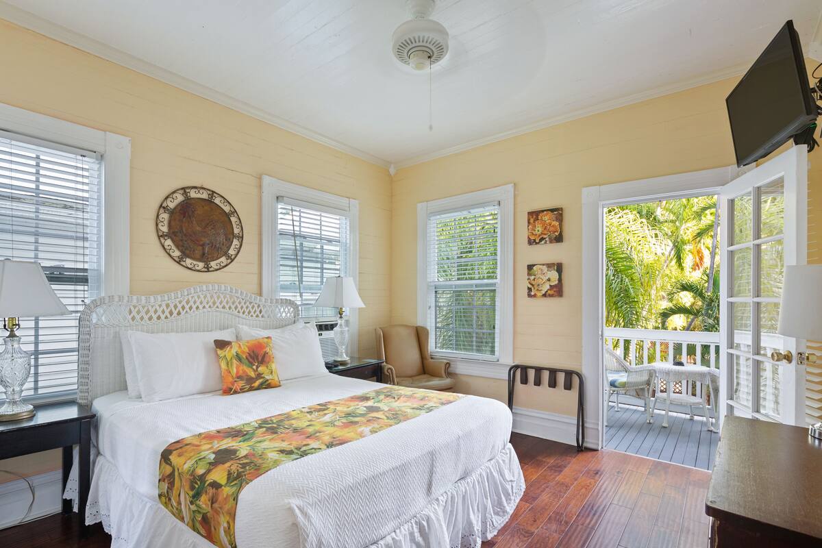 A bedroom with a bed, a chair, a desk, and a balcony with a view of greenery.