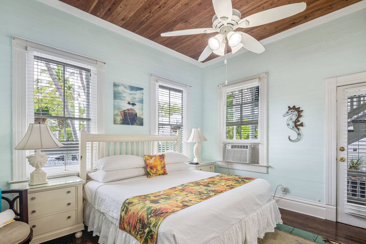 A bedroom with a bed, nightstands, a ceiling fan, and a door with a window.