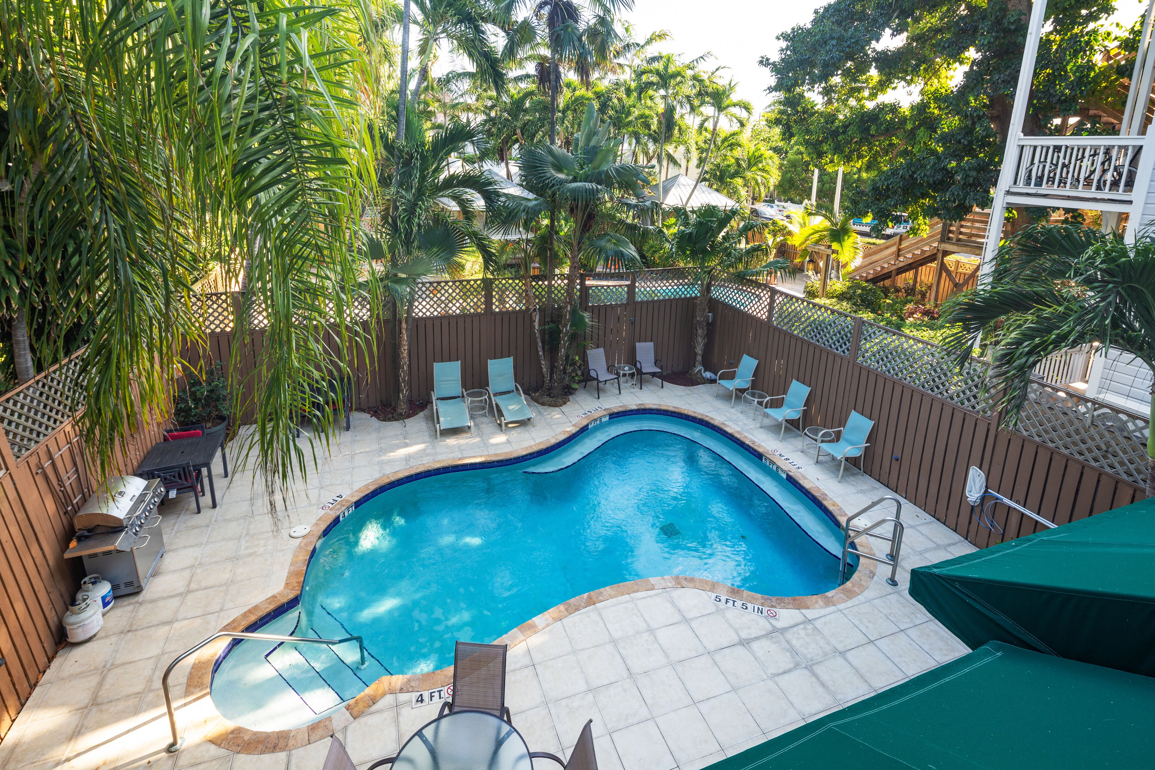 A swimming pool with a wooden deck, lounge chairs, and a barbecue area.