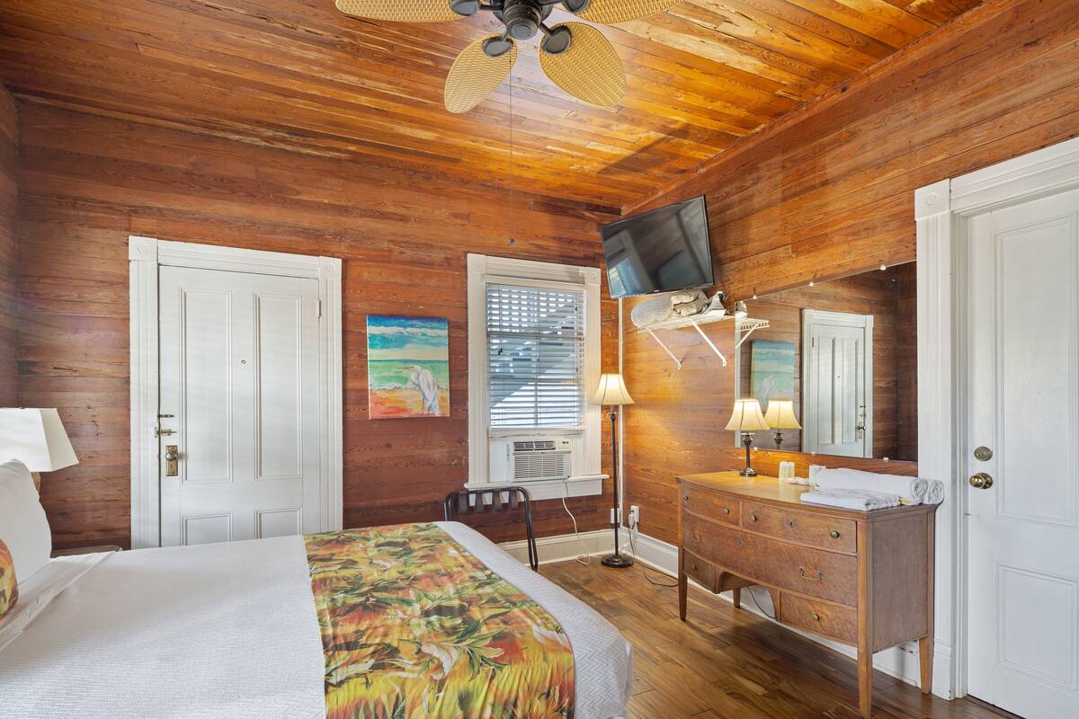 A wooden-paneled room with a bed, dresser, and television.
