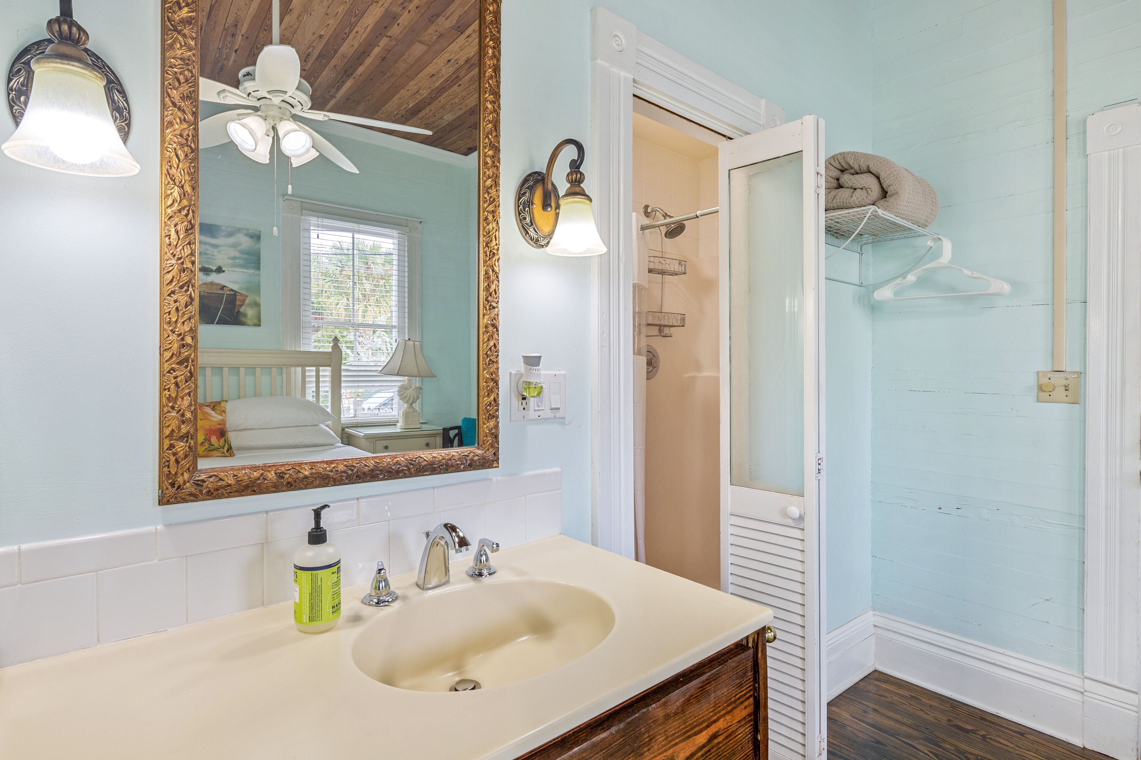 A bathroom with a large mirror, a sink, a shower, and a ceiling fan.