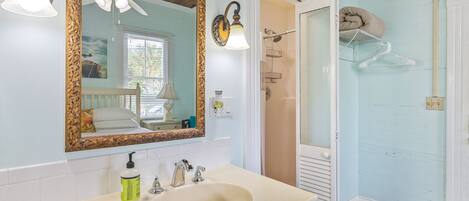 A bathroom with a large mirror, a sink, a shower, and a ceiling fan.