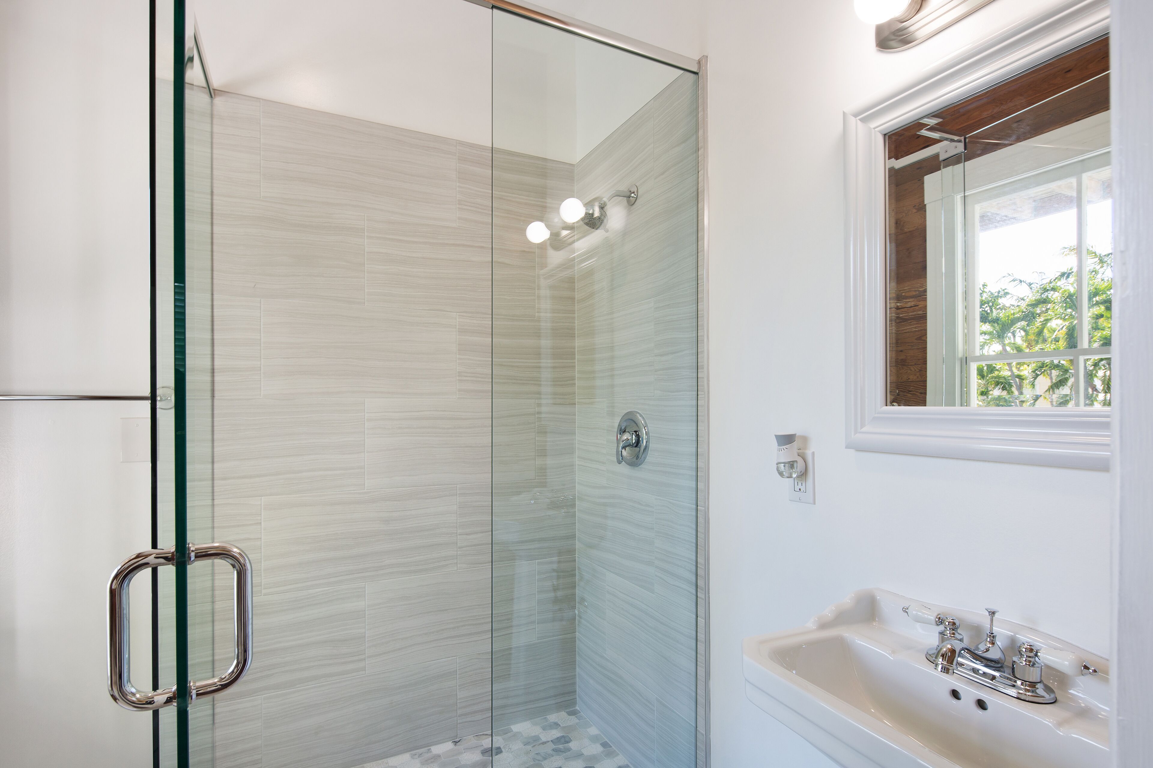 Une salle de bain moderne avec une douche à parois de verre, un lavabo blanc doté de robinetterie chromée et une fenêtre située au-dessus du lavabo.