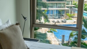 A bedroom with a large window overlooking a modern pool area with lounge chairs and palm trees. - Newly Built, Hottest Condo at "Sky Ala Moana" 10th Floor  1 Bedroom (SAW1005) (Honolulu)