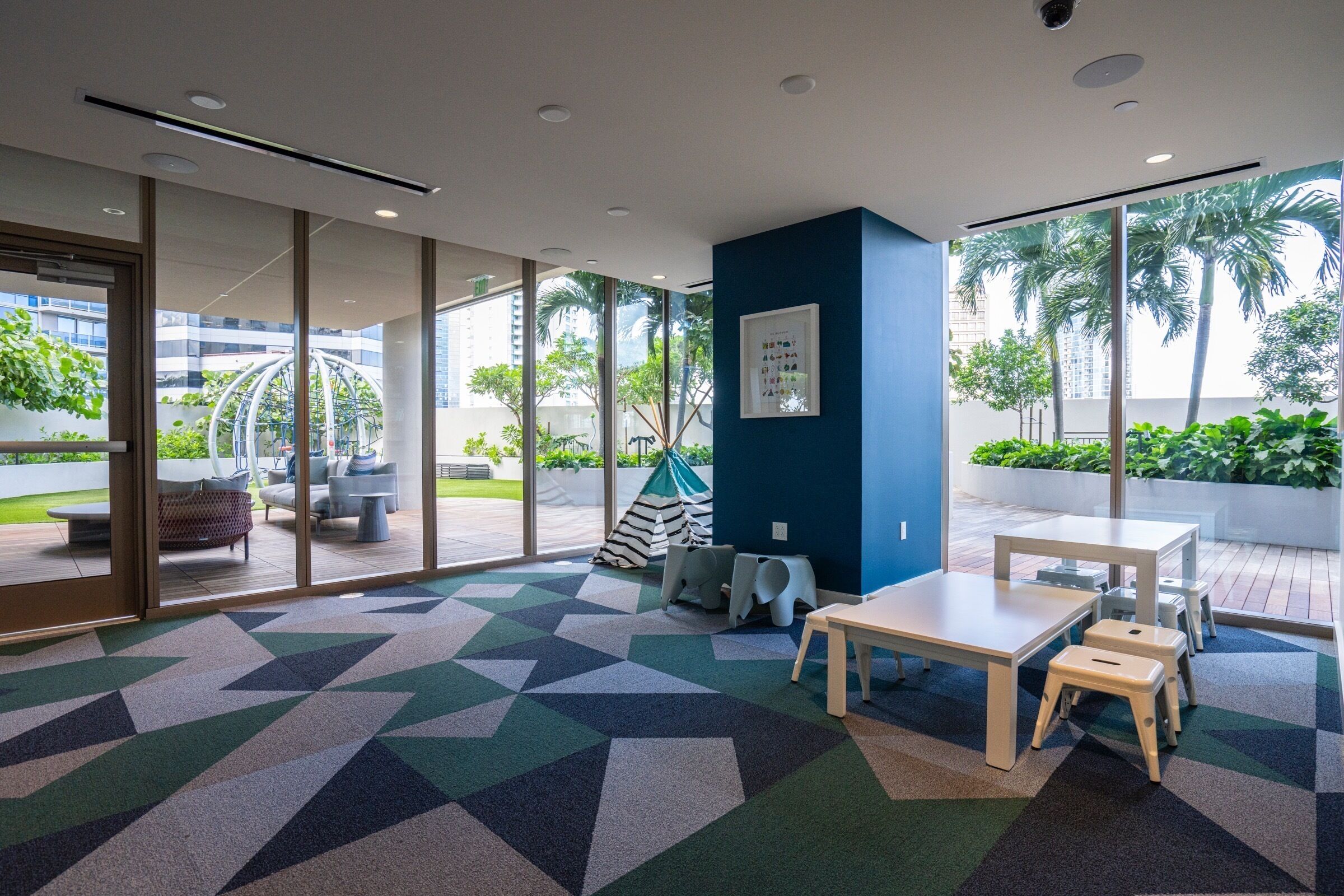 A modern indoor space with a geometric patterned carpet, a white table with a bench, and a blue accent wall.