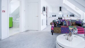A modern living room with a round coffee table, a colorful sofa, and a kitchen in the background. - The Penthouse - Luxury 1 Bed - Panorama - Tenby (Tenby)
