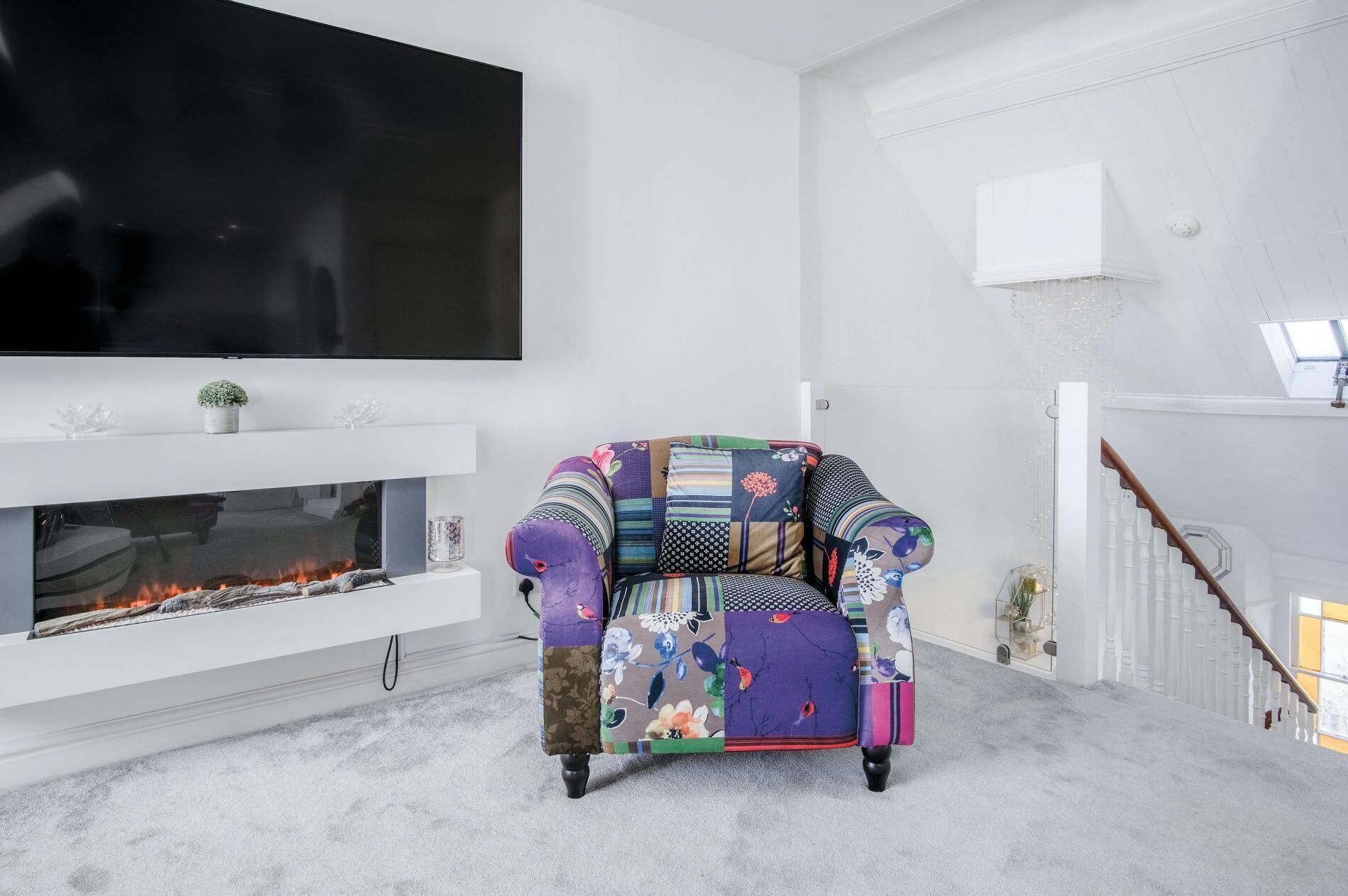 Un salon avec une cheminée, un fauteuil coloré, un téléviseur à écran plat et un escalier.