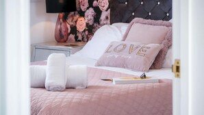 A neatly made bed with pink bedding, a pillow with "LOVE lives here" text, and a book with a pen on it. - The Penthouse - Luxury 1 Bed - Panorama - Tenby (Tenby)