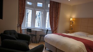 Une chambre d’hôtel avec un lit, une chaise, une petite table et une fenêtre avec des rideaux.