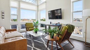 A modern living room with large windows, a flat-screen TV, and a cozy seating area. - Skyline Penthouse | Espadin LoHi (Denver)
