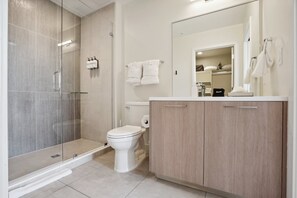A modern bathroom with a glass-enclosed shower, a white toilet, and wooden cabinets. - Skyline Penthouse | Espadin LoHi (Denver)