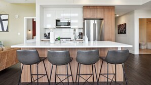 A modern kitchen with a central island, stainless steel appliances, and black bar stools. - Skyline Penthouse | Espadin LoHi (Denver)