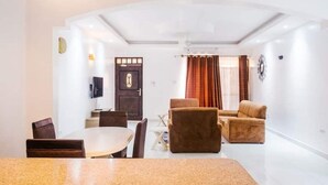 Una sala de estar moderna con comedor, un conjunto de sofás y un televisor montado en la pared.