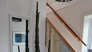 Una escala amb barana de fusta i paret blanca amb mirall i una planta de cactus.