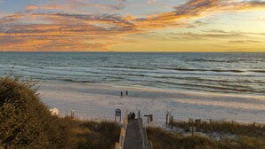 Una spiaggia con una passerella in legno che conduce all'acqua, una battigia sabbiosa e un cielo al tramonto.
