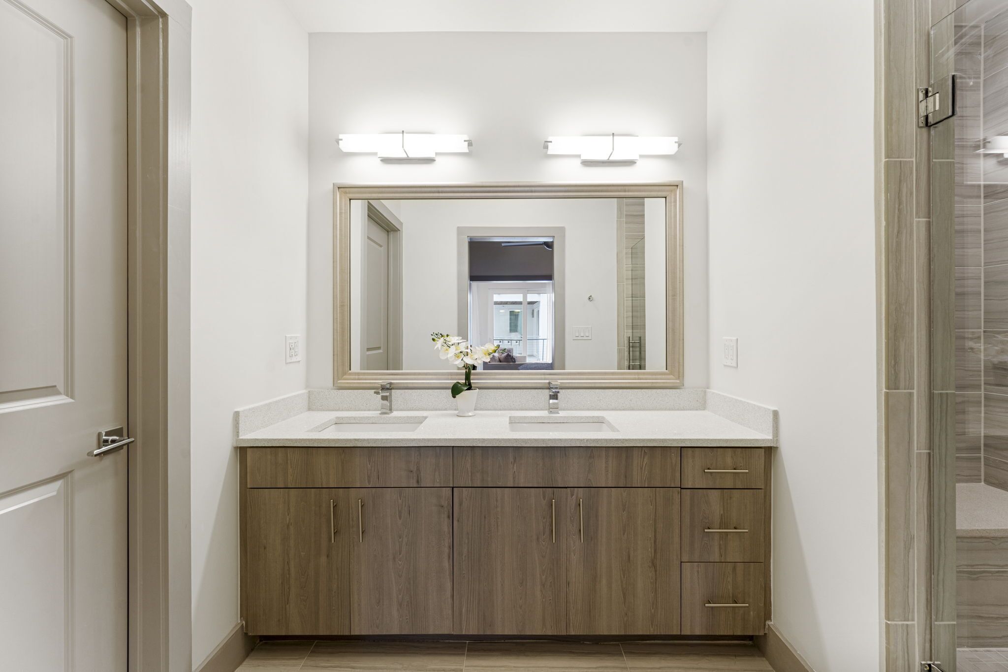 A bathroom with two sinks, wooden cabinets, and a large mirror with lights above.